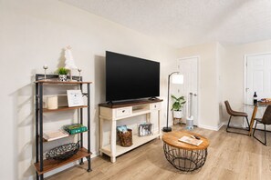 A living room with a flat-screen TV, a coffee table, a bookshelf, a lamp, and a dining area with chairs. - Pet-Friendly King Bed Stay w/ Screened Porch // Pigeon Forge (Pigeon Forge)