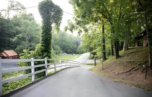 A paved road with a white fence on one side and a grassy area with trees on the other.