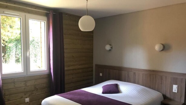 Een slaapkamer met een bed, een nachtkastje, een hanglamp, een raam met gordijnen en een houten wand.