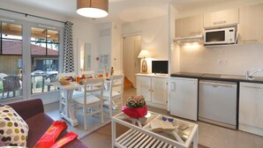 Een ruimtelijk ingerichte leefruimte met een kitchenette, een eethoek en een glazen deur naar een terras.