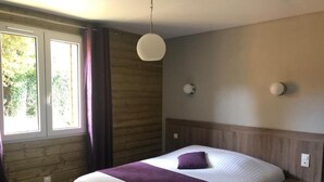 Een slaapkamer met een bed, een raam met gordijnen, een wandlamp en een houten hoofdbord.
