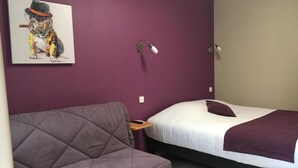 A room with a bed, a sofa, a wall-mounted lamp, and a painting of a dog. - Logis Hotel le Val Sarah (Bardouville)