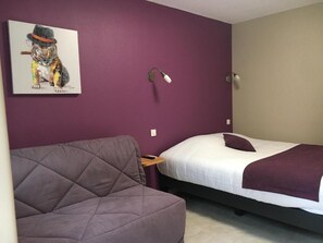 A room with a bed, a sofa, a wall-mounted lamp, and a painting of a dog. - Logis Hotel le Val Sarah (Bardouville)