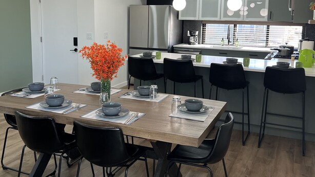 A modern kitchen with a central island, black chairs, and a dining table set for six. - LuXury ZeN ZoNE (No Cleaning fee, King size bed). (Omaha)