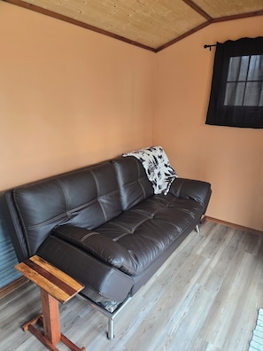 A brown leather sofa with a patterned throw pillow, a wooden coffee table, and a window with a black curtain. - Your lakeside oasis awaits: perfect for families and fun! (Hackensack)