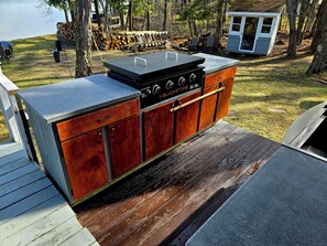 An outdoor kitchen with a built-in grill, wooden cabinets, and a deck.