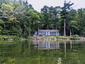 Una cabaña junto al lago con muelle, rodeada de un bosque frondoso.