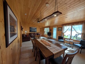 A wooden interior with a dining table, chairs, a sofa, and a television.