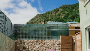 A swimming pool with two lounge chairs, a stone wall, and a view of a green hillside. - Topaz Apartment Villa - Piton View (soufriere)