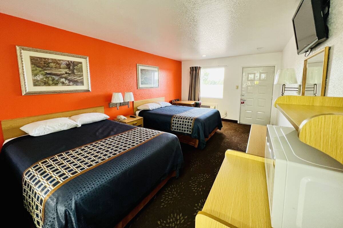 A hotel room with two beds, a TV, a desk, and a bathroom.
