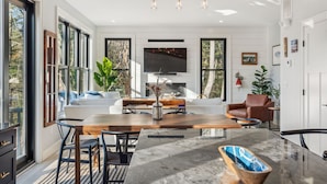 A modern living room with a large TV, a fireplace, and a dining area with a marble table.