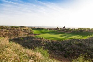 A golf course with a bunker, a water hazard, and a distant building.