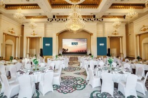 A banquet hall with round tables, white chairs, and a large screen at the front. - Avanna Hotel (Jungar Banner)