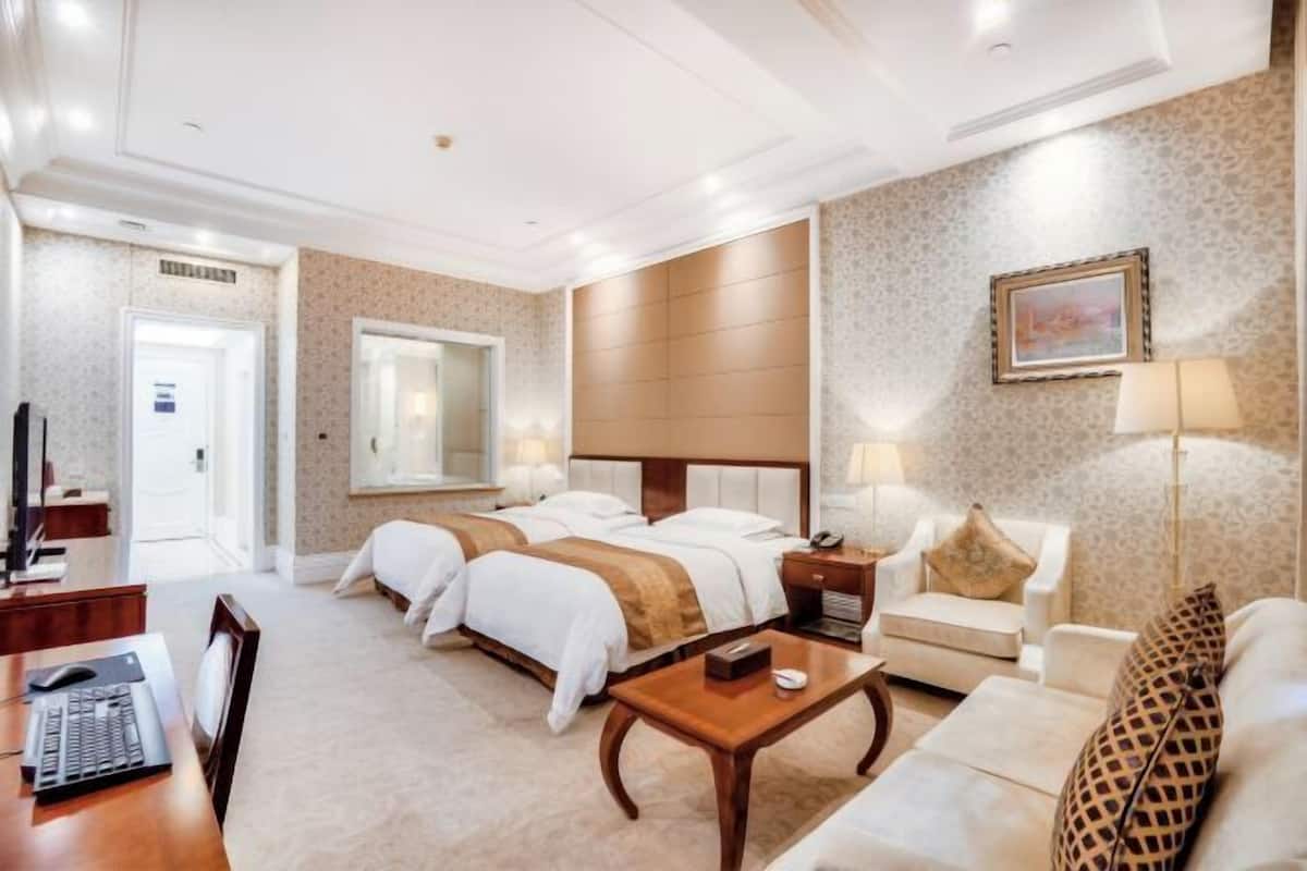 Habitación de hotel con dos camas, un escritorio, una silla, una mesita de centro y un sofá.