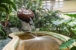 A water feature with a stone sculpture, surrounded by lush greenery. - Avanna Hotel (Jungar Banner)