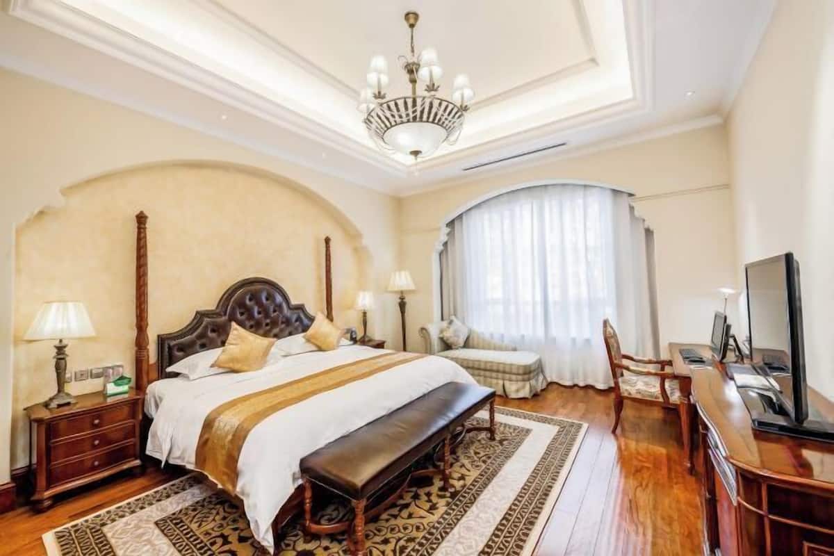 Habitación de hotel con una cama grande, un banco, un escritorio con una computadora, un televisor y una araña.