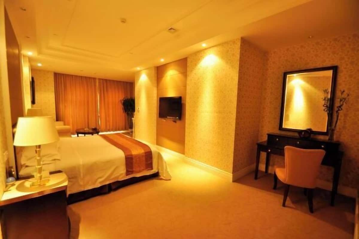 Una habitación de hotel con cama, escritorio, silla, televisor y espejo.