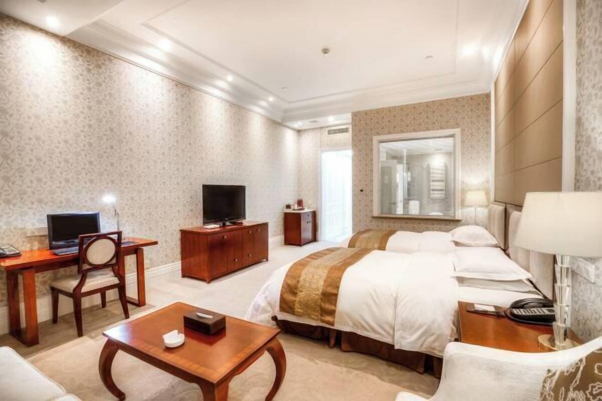 Habitación de hotel con cama, escritorio con televisor, silla, mesita de noche y lámpara.