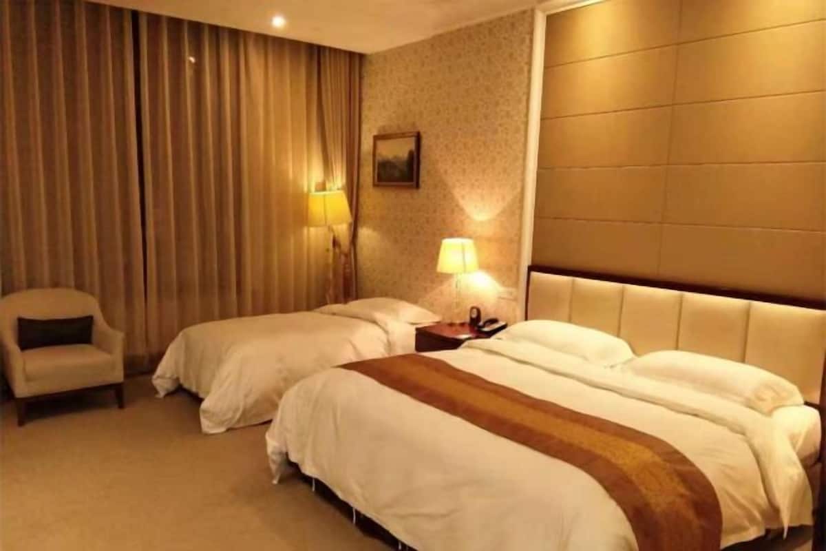 Una habitación de hotel con dos camas, una silla, una lámpara y un cuadro en la pared.