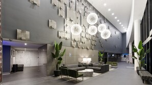 Eine moderne Lobby mit Grau- und Weißtönen, ausgestattet mit einer Rezeption, einer Sitzecke mit Sofas und einem Couchtisch sowie dekorativen Wandbildern.