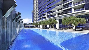Ein Schwimmbad neben einem modernen Gebäude mit Balkonen und blauem Himmel.