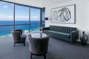 A modern room with a large window, a grey sofa, two armchairs, a round table, and a large abstract painting.