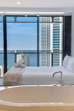 A modern hotel room with a large bed, a bathtub, and a view of the city skyline.