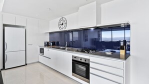 A modern kitchen with a large window, stainless steel appliances, and a clock on the wall. - 53rd Floor - Sky High Apartment in Circle on Cavil (Gold Coast)