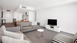 A modern living room with a grey sofa, a striped armchair, a small round coffee table, a flat-screen TV on a white stand, and a dining area in the background. - Charming Level 35 Central Getaway (Gold Coast)
