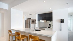 A modern kitchen with a central island, bar stools, stainless steel appliances, and a phone on the wall. - Charming Level 35 Central Getaway (Gold Coast)