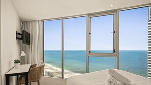 Une chambre d’hôtel équipée d’un lit, d’un bureau, d’une chaise, d’une télévision et de grandes fenêtres donnant sur l’océan.