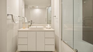 Une salle de bain moderne avec une douche à parois de verre, un lavabo blanc et un grand miroir.
