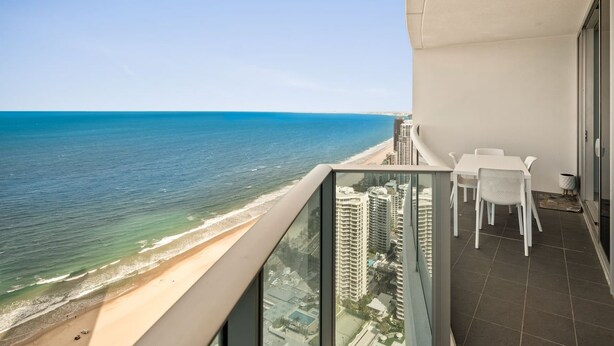 Un balcon avec vue sur la plage et l’océan, une table avec des chaises et une poubelle.