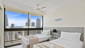 A hotel room with two beds, a ceiling fan, a nightstand, and a view of tall buildings. - Luxury Oceanview Apartment with Balcony (Surfers Paradise)