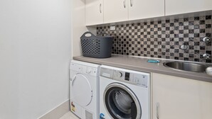 A modern laundry room with a washing machine and dryer, a sink, and a tiled backsplash. - Luxury Oceanview Apartment with Balcony (Surfers Paradise)