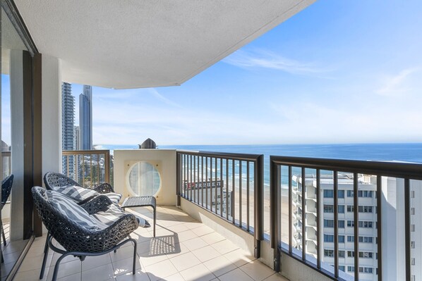 A balcony with wicker chairs, a small table, and a view of the ocean and buildings. - Full Ocean View Lvl21- 2Bed2Bath -Long Beach Apt (Surfers Paradise)