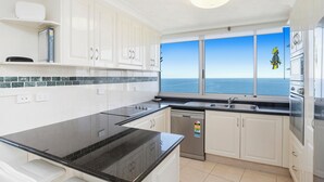 A modern kitchen with white cabinets, a black countertop, and a view of the ocean through large windows.