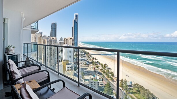 A balcony with wicker furniture overlooking a beach and cityscape. - 28th Floor Oceanfront Bliss in Surfers Paradise (Surfers Paradise)