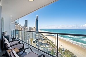 A balcony with wicker furniture overlooking a beach and cityscape. - 28th Floor Oceanfront Bliss in Surfers Paradise (Surfers Paradise)