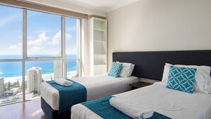 A hotel room with two beds, a large window with a view of the ocean and buildings, and a ceiling light. - Sleeps 7 - High Level Ocean View Apt - Chevron! (Surfers Paradise)