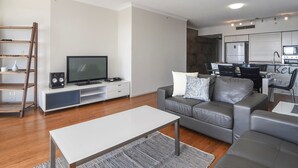 A modern living room with a grey sofa, a white coffee table, and a TV on a white cabinet. - Sleeps 7 - High Level Ocean View Apt - Chevron! (Surfers Paradise)