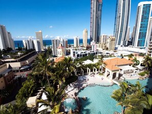Een resort met een groot zwembad, palmbomen en hoge gebouwen op de achtergrond.