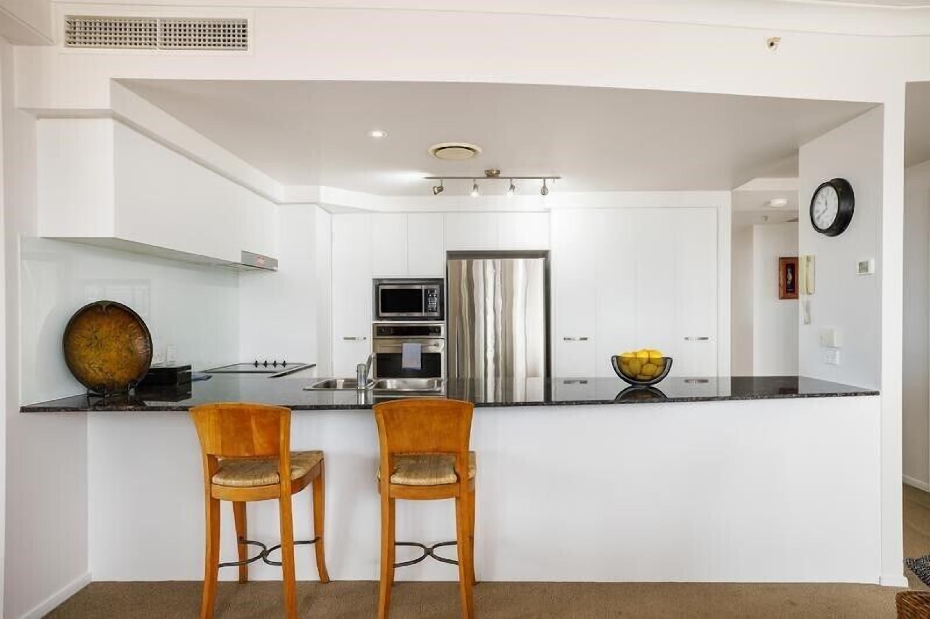 A modern kitchen with white cabinetry, stainless steel appliances, and two wooden bar stools.