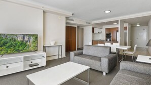 Una sala de estar moderna con un televisor de pantalla plana, un sofá gris, una mesa de centro blanca y una zona de comedor con una mesa y sillas blancas.