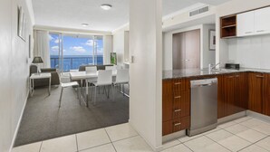 Cocina moderna con vista al océano, comedor con mesa y sillas, y un pequeño balcón con vistas.