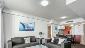 Een moderne woonkamer met twee grijze banken, een glazen salontafel en een schilderij van een steiger.