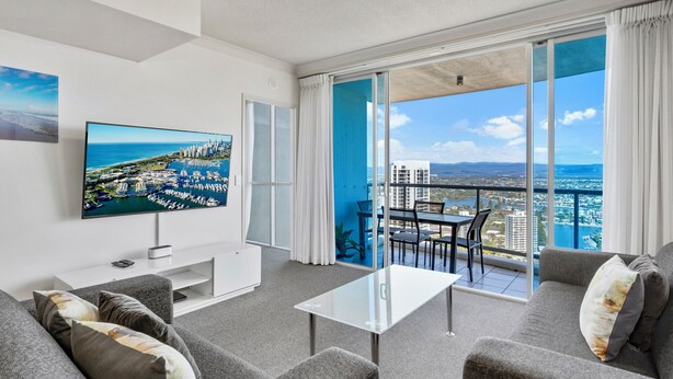 Een moderne woonkamer met een grote televisie, comfortabele zithoek en een balkon met uitzicht op de stad.