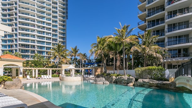 Piscina de resort con agua cristalina, rodeada de palmeras y un edificio grande con balcones.