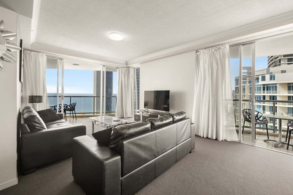 Una sala de estar moderna con sofá, televisor y balcón con cortinas.