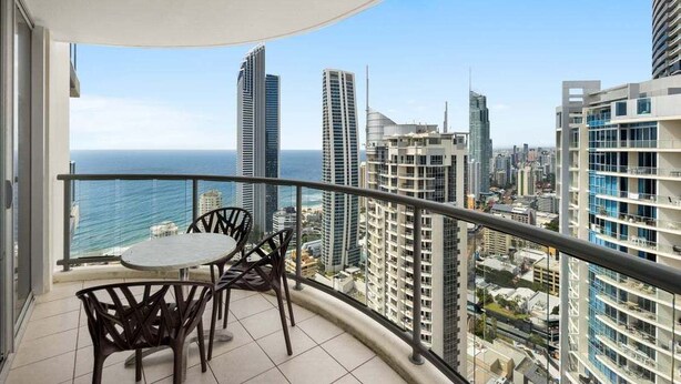 Un balcon offrant une vue sur l’océan et le paysage urbain, avec des bâtiments modernes et un ciel dégagé.